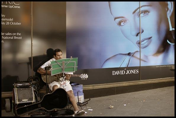 a guitar palyer with his microphone and amp set-up before a cosmetics poster at David Jones