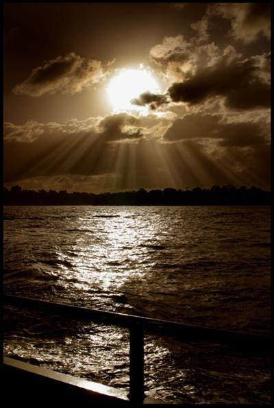 Cloudscape with setting sun and dramatic sun-rays and the sun reflecting on the water
